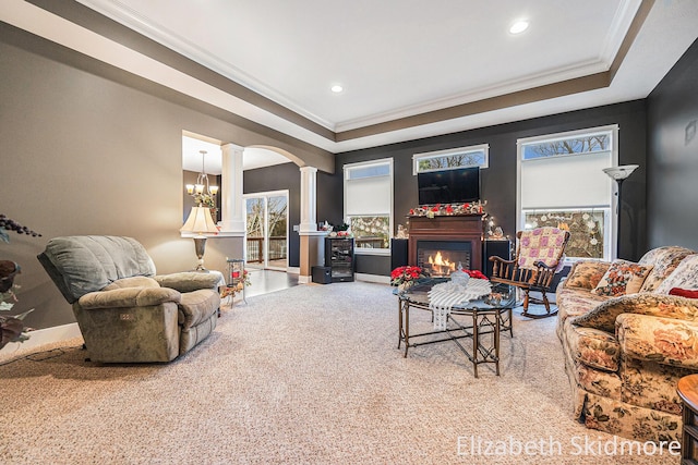 living room featuring a notable chandelier, decorative columns, crown molding, light colored carpet, and a tray ceiling