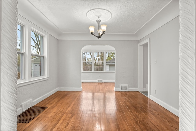 unfurnished dining area with hardwood / wood-style floors, a textured ceiling, and a notable chandelier