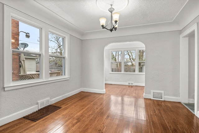 unfurnished dining area featuring hardwood / wood-style floors, a textured ceiling, a wealth of natural light, and a chandelier