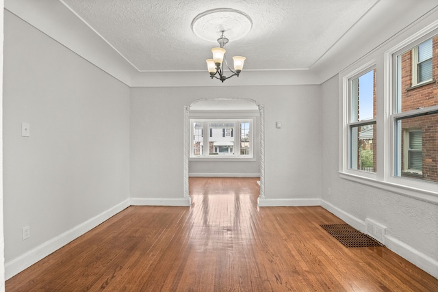 unfurnished dining area with hardwood / wood-style floors, a healthy amount of sunlight, a textured ceiling, and an inviting chandelier