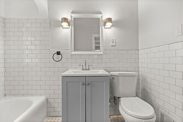 bathroom featuring vanity, a bathtub, tile patterned floors, toilet, and tile walls