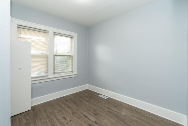 empty room with dark wood-style flooring, visible vents, and baseboards