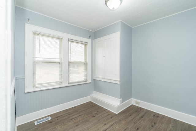 unfurnished room featuring baseboards, visible vents, dark wood-type flooring, and ornamental molding