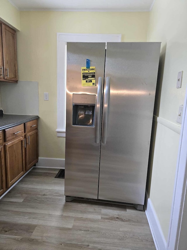 kitchen featuring dark countertops, light wood-style flooring, ornamental molding, stainless steel fridge, and baseboards