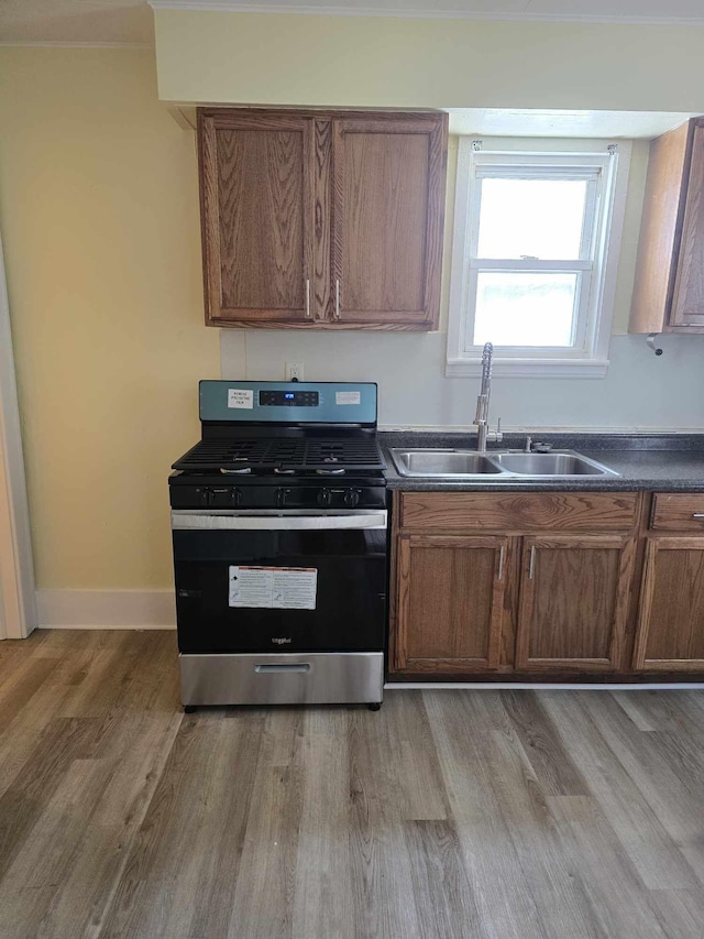 kitchen with a sink, light wood-style floors, brown cabinets, dark countertops, and stainless steel range with gas stovetop