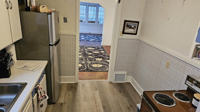 kitchen with white cabinets, stainless steel appliances, tile walls, and light hardwood / wood-style floors