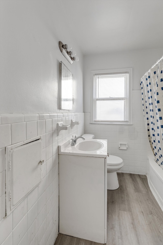 full bathroom featuring wood-type flooring, toilet, shower / bath combo with shower curtain, vanity, and tile walls