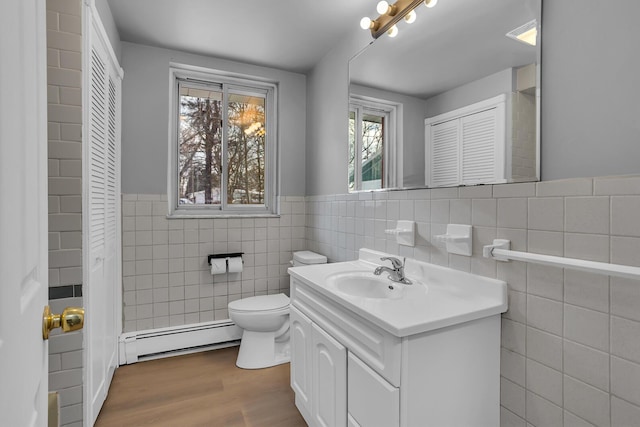 bathroom featuring vanity, a baseboard heating unit, tile walls, hardwood / wood-style floors, and toilet