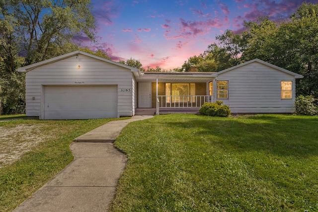 ranch-style home with covered porch, a yard, and a garage