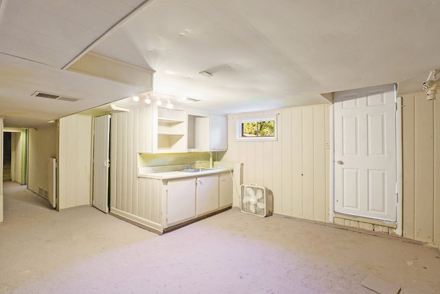 kitchen with white cabinetry, wood walls, and sink