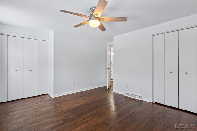 unfurnished bedroom with dark hardwood / wood-style floors, ceiling fan, and multiple closets