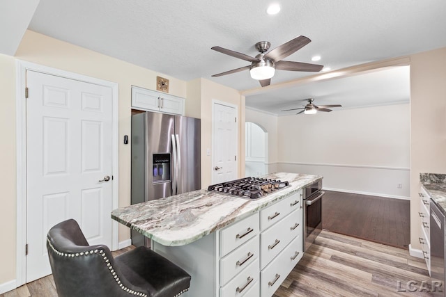 kitchen with a breakfast bar, stainless steel appliances, a center island, light hardwood / wood-style floors, and white cabinetry