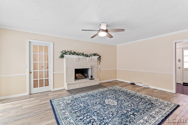 living room with ceiling fan, light hardwood / wood-style flooring, crown molding, a textured ceiling, and a fireplace