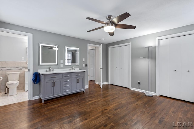 interior space with ceiling fan, wood-type flooring, toilet, vanity, and tile walls