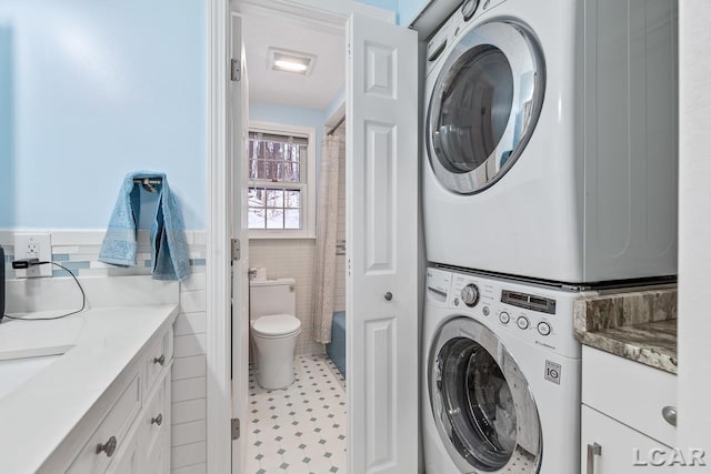 washroom featuring stacked washer / dryer and tile walls