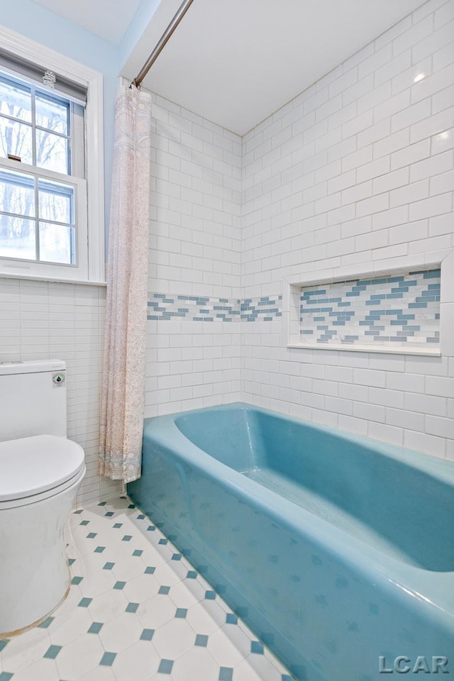 bathroom with toilet, tile walls, and shower / tub combo with curtain