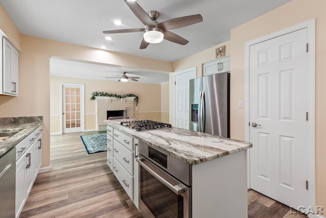 kitchen with appliances with stainless steel finishes, a textured ceiling, white cabinets, a center island, and light hardwood / wood-style floors