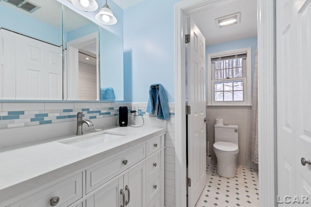 bathroom featuring toilet, vanity, tile patterned floors, and tile walls