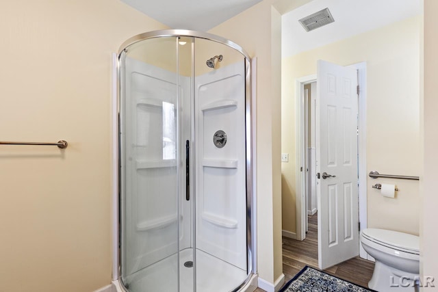 bathroom featuring hardwood / wood-style floors, a shower with shower door, and toilet