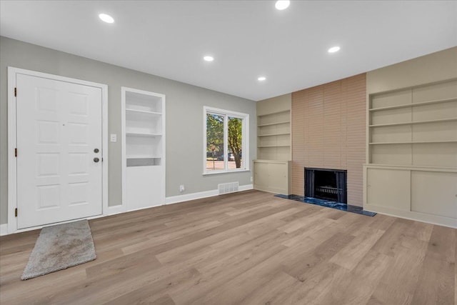 unfurnished living room with built in shelves, a large fireplace, and light hardwood / wood-style floors