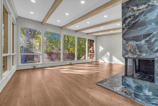 unfurnished living room featuring a multi sided fireplace, beamed ceiling, and wood-type flooring