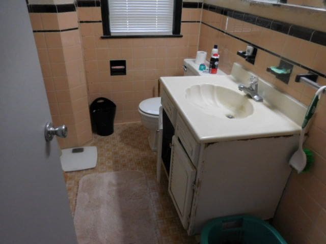 bathroom with tile patterned flooring, vanity, toilet, and tile walls