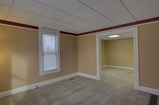 empty room featuring a drop ceiling, light colored carpet, and ornamental molding