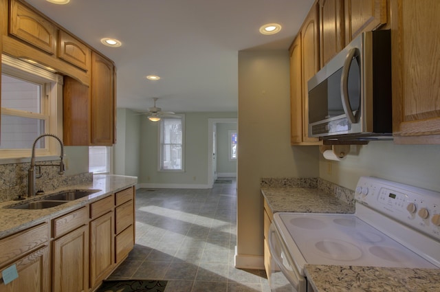 kitchen featuring electric range, ceiling fan, light stone counters, and sink