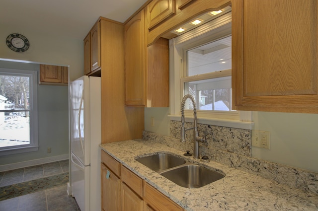 kitchen featuring light stone counters, sink, white fridge, and plenty of natural light