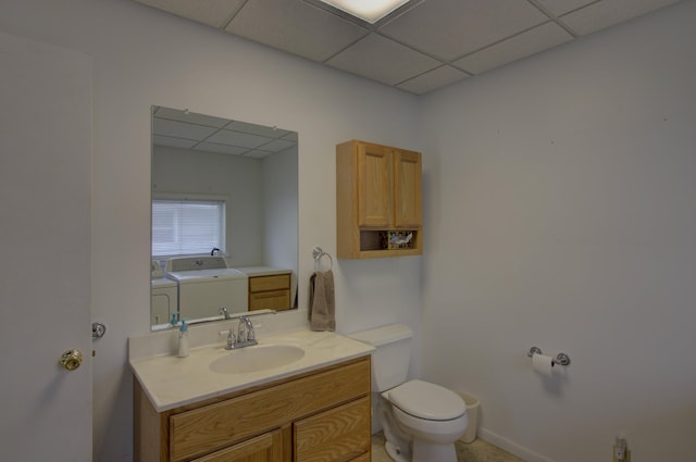 bathroom with a drop ceiling, vanity, washer and dryer, and toilet