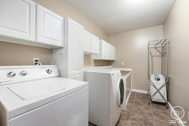 laundry room with cabinets, a textured ceiling, dark tile patterned flooring, and washing machine and clothes dryer