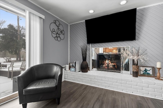 living area with a brick fireplace, wood walls, ornamental molding, and hardwood / wood-style flooring