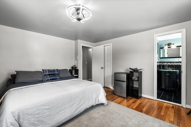 bedroom featuring hardwood / wood-style flooring, stainless steel fridge, a closet, and connected bathroom