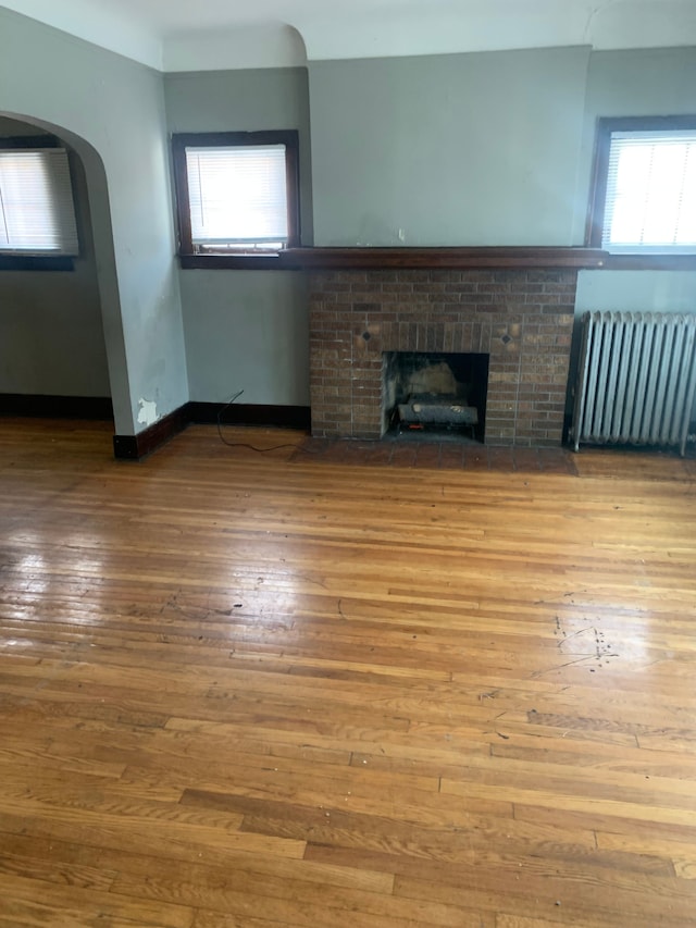 unfurnished living room featuring a fireplace, radiator heating unit, and wood-type flooring