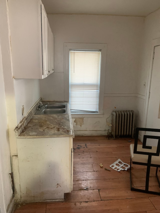 kitchen with white cabinets, light wood-type flooring, sink, and radiator