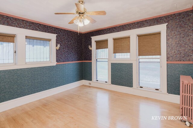 spare room featuring radiator, wood finished floors, baseboards, wallpapered walls, and ceiling fan