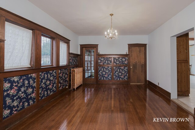 unfurnished dining area with baseboards, a notable chandelier, hardwood / wood-style floors, and radiator heating unit