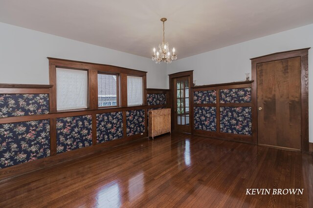 unfurnished room featuring a chandelier, wood finished floors, and radiator heating unit