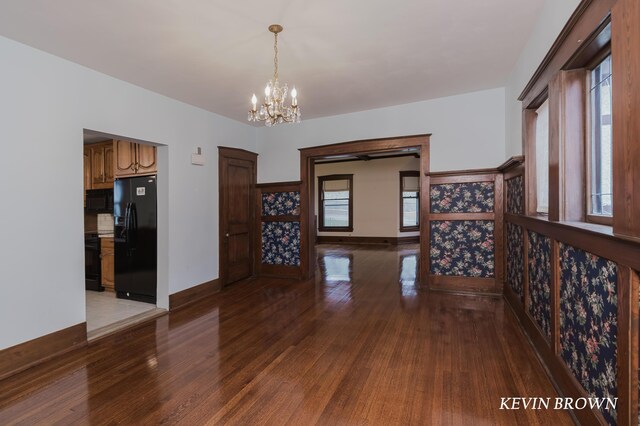 unfurnished dining area featuring plenty of natural light, baseboards, an inviting chandelier, and wood finished floors