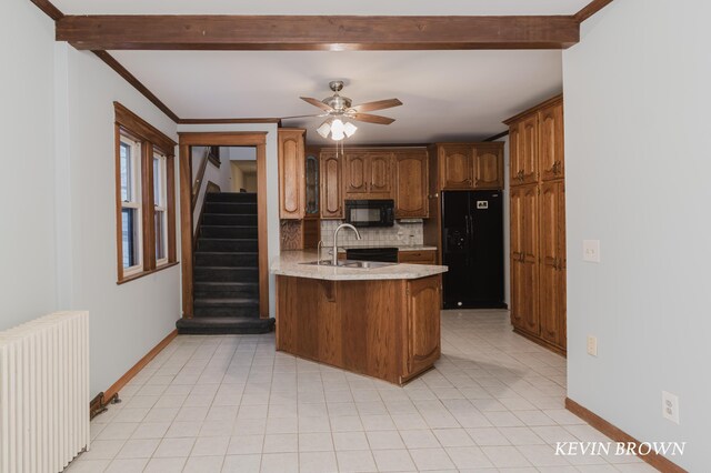 kitchen featuring beam ceiling, a peninsula, radiator heating unit, a sink, and black appliances