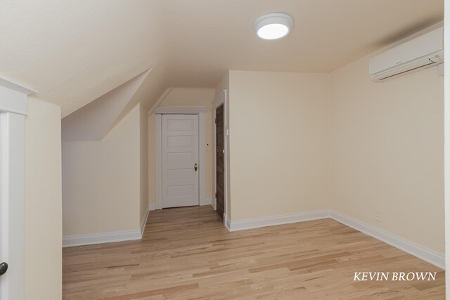 additional living space featuring baseboards, lofted ceiling, an AC wall unit, and light wood-style flooring