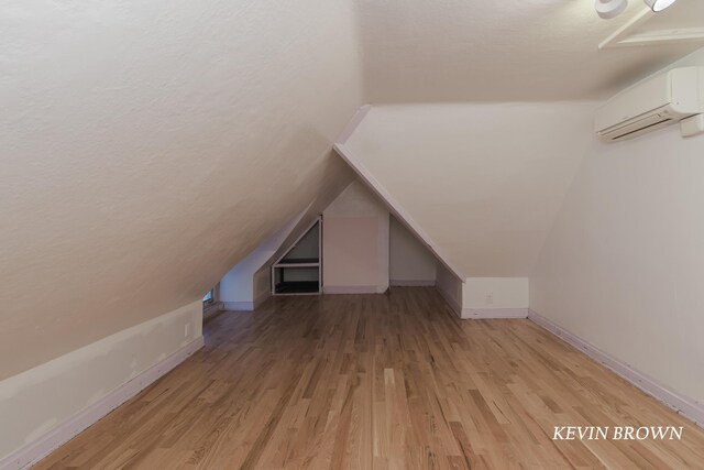 bonus room featuring light wood-type flooring, baseboards, an AC wall unit, and vaulted ceiling