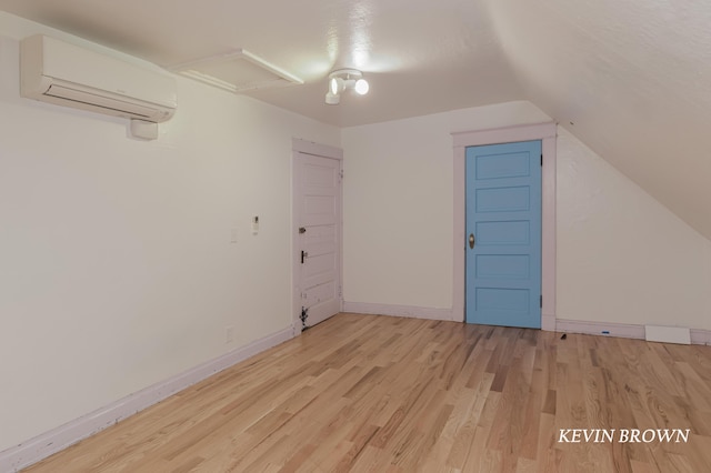 additional living space with baseboards, attic access, lofted ceiling, a wall unit AC, and light wood-style floors