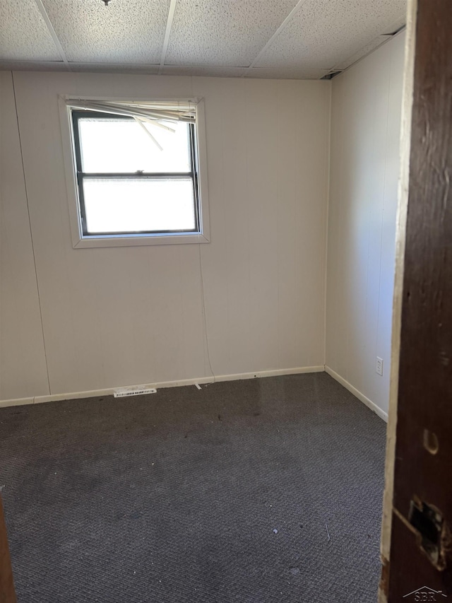 unfurnished room featuring a drop ceiling and dark carpet