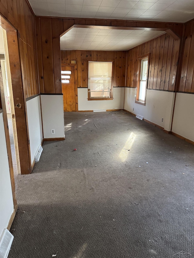 carpeted empty room featuring wood walls