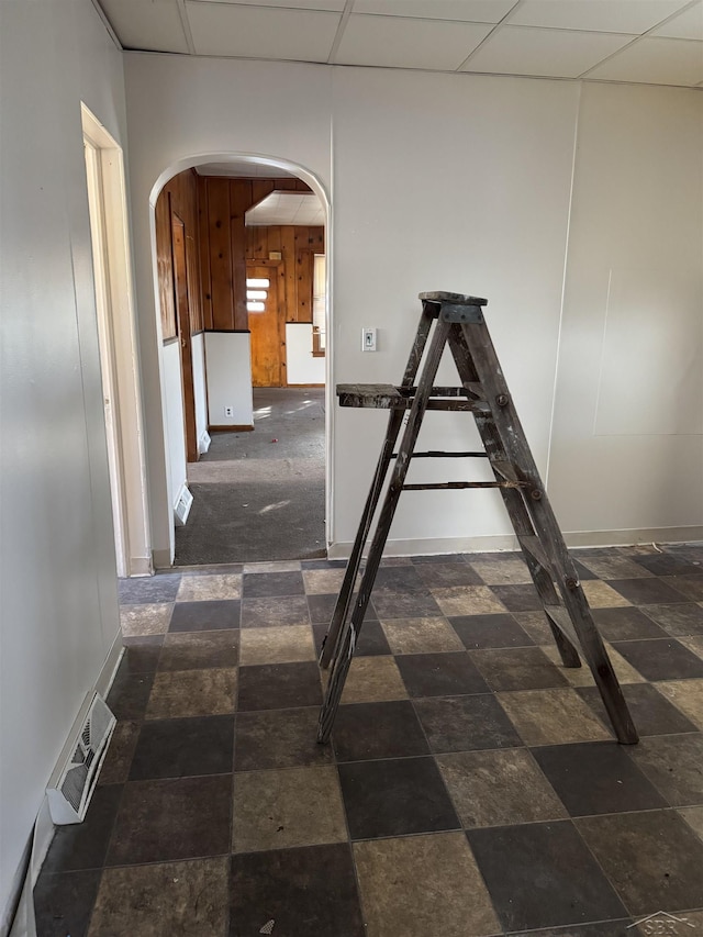 hallway featuring a paneled ceiling and wooden walls