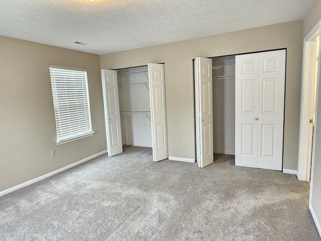 unfurnished bedroom featuring multiple closets, light carpet, and a textured ceiling