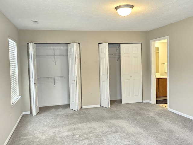 unfurnished bedroom with ensuite bath, multiple closets, light colored carpet, and a textured ceiling