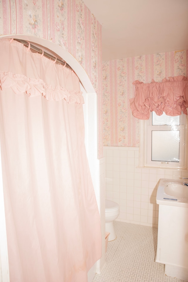 bathroom featuring tile patterned flooring, vanity, toilet, and tile walls