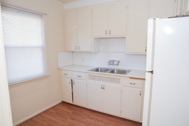 kitchen with a wealth of natural light, sink, white fridge, white cabinets, and light wood-type flooring